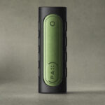 PAX Flow Grip Sleeve in black and green on a textured grey-green studio background.