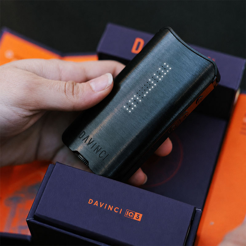 Black DaVinci IQ3 Vaporizer held above branded product packaging