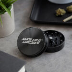 Black Santa Cruz Shredder 2-piece grinder open on a desk with dry herb nearby.