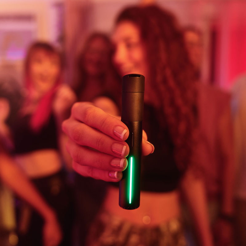 Person holding the Puffco Pivot portable vaporizer with glowing LED light in a colourful nightlife setting.