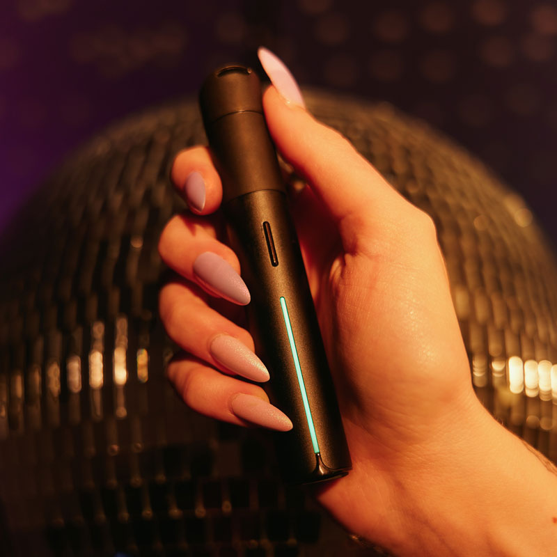 Hand holding the Puffco Pivot vaporizer with glowing LED light in front of a disco ball background.