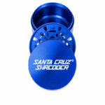 Blue Santa Cruz Shredder 3-piece grinder opened to show the lid, grinding teeth and chamber on a white background.