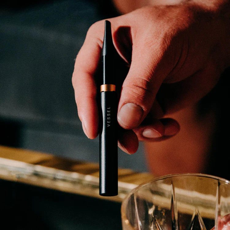 Hand holding Vessel Core 510 battery beside glass smoking accessory.