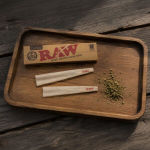 RAW rolling papers and pre-rolled cones on a Marley Natural wooden rolling tray with ground herb on a rustic wooden table