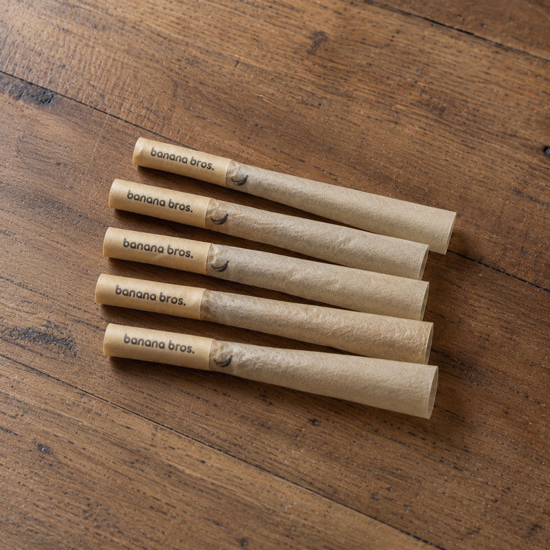 Five Banana Bros short pre-rolled cones with natural paper variations arranged on a rustic wooden table surface.