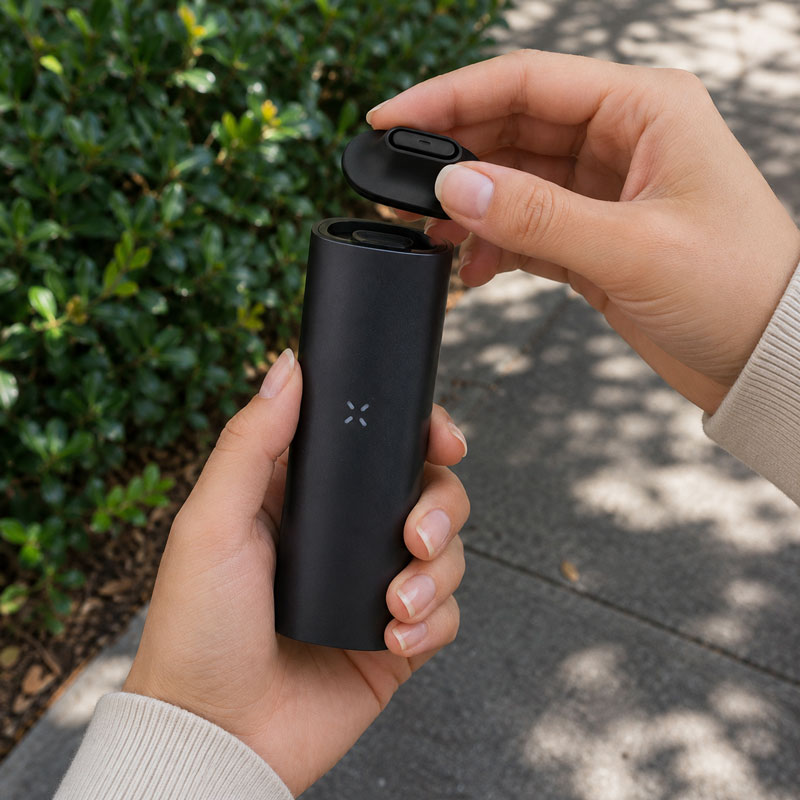 Woman attaching a raised PAX 4 mouthpiece outdoors with blurred garden background