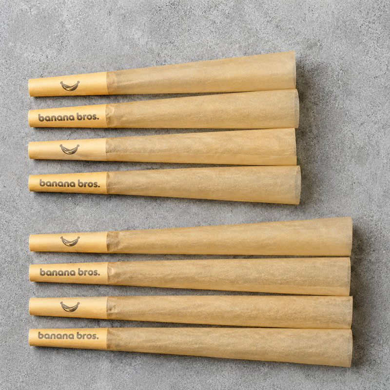 Top-down view of eight Banana Bros unbleached pre-rolled cones arranged on a textured grey surface.