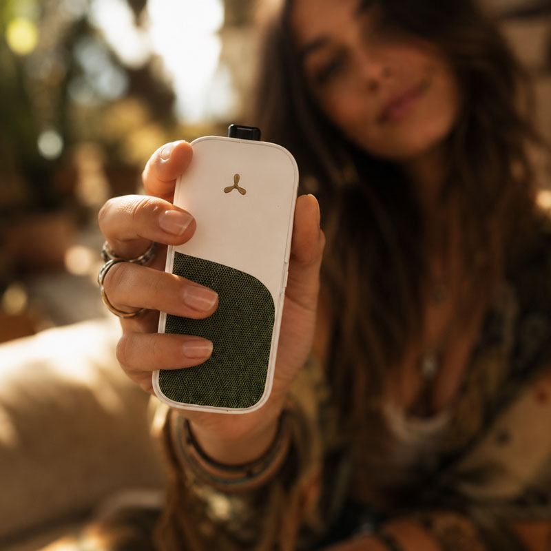 Woman holding a white AirVape Legacy CORE vaporizer in a close-up outdoor lifestyle setting