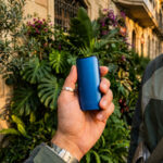 Blue DaVinci IQ Core vaporizer held in a hand outdoors against a leafy background