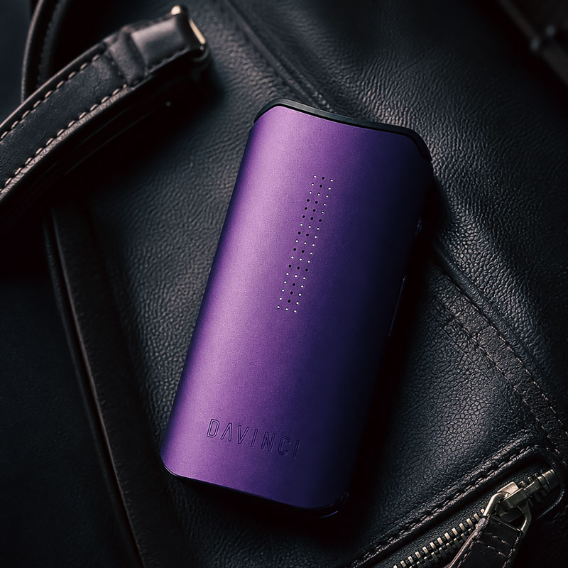 Purple DaVinci IQ Core vaporizer resting on a black leather bag