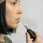 Close-up of a woman exhaling vapour while holding the G Pen 510 OG battery