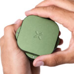 PAX Grinder in Greenstone held in both hands with the magnetic lid partially turned