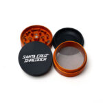 Santa Cruz Shredder Split Series orange and black grinder opened to show the teeth, screen and collection chamber