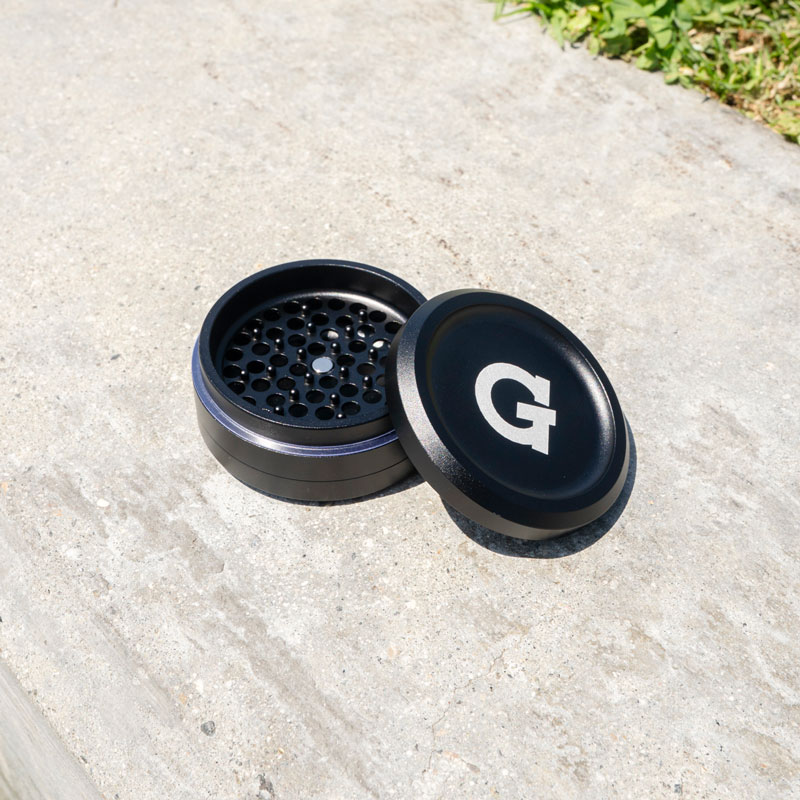 G Pen 3-Piece Slim Grinder open outdoors with the branded lid beside the grinding chamber