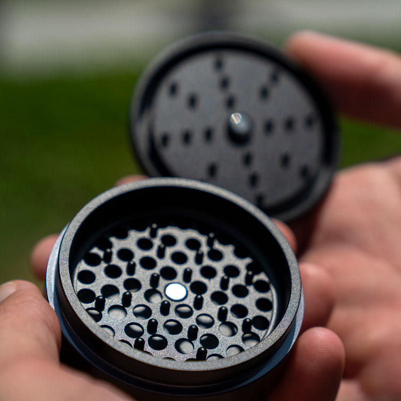 Open G Pen Slim Grinder held in hand showing the perforated grinding chamber and magnetic lid
