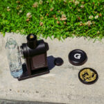 G Pen 3-Piece Slim Grinder beside a vaporizer setup with ground dry herb in the collection chamber
