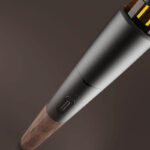 Angled close up of the Vessel Craftsman 510 Battery showing its smooth metal housing, control button and natural walnut grain